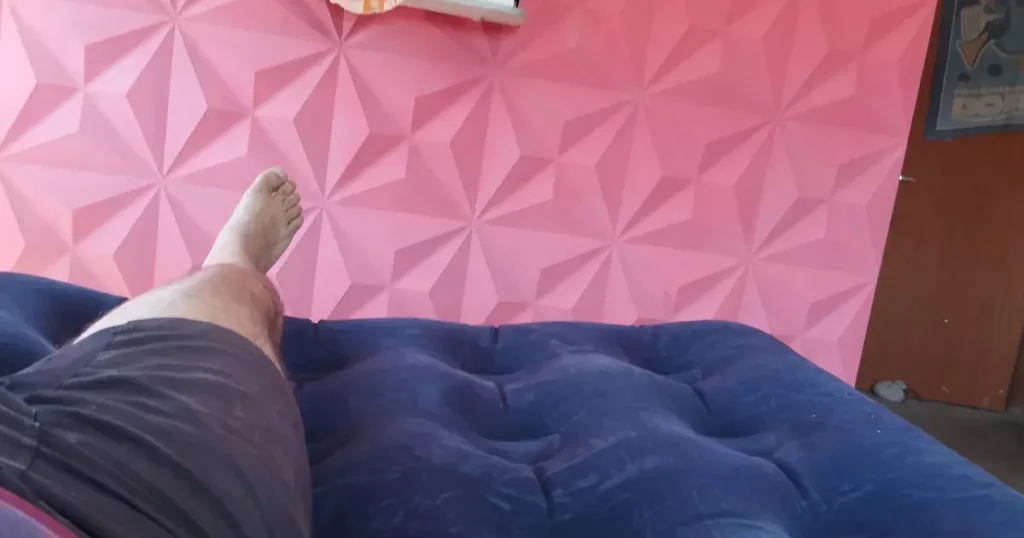 Pessoa descansando em colchão inflável azul com parede geométrica rosa ao fundo
